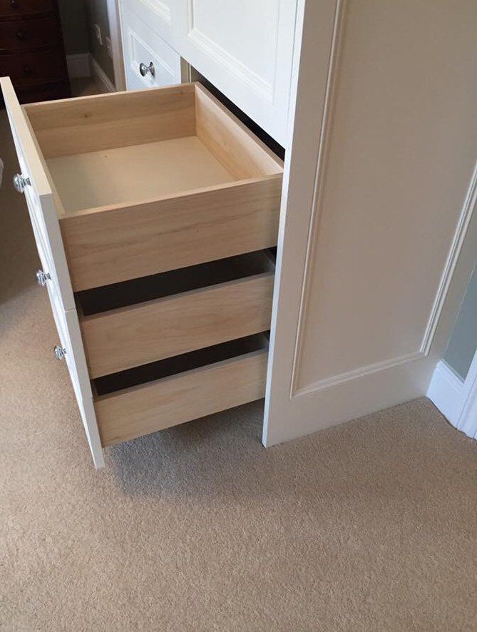 A wooden drawer is open in a white cabinet.