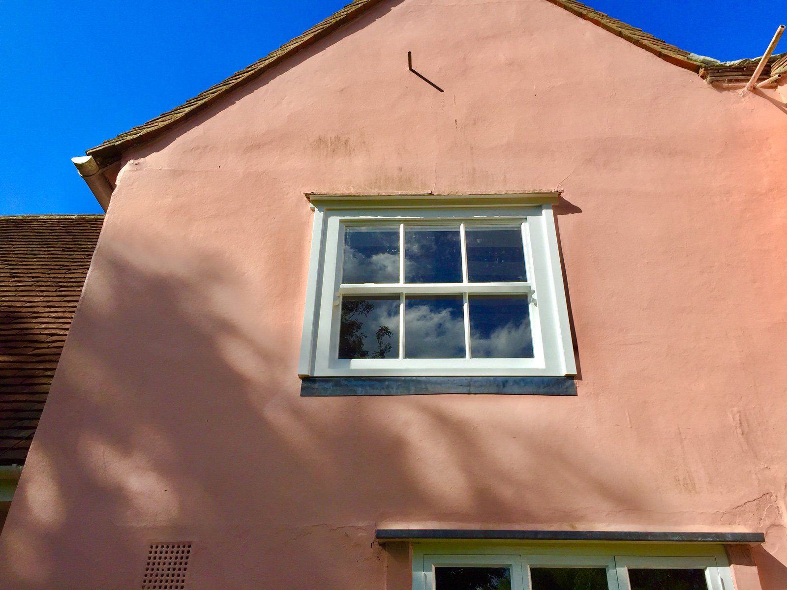 A pink house with a white window and a blue sky in the background