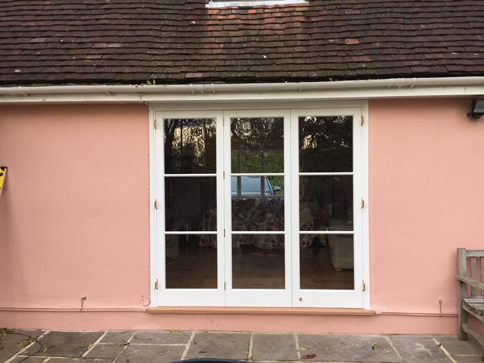 A pink house with white french doors and a bench in front of it.