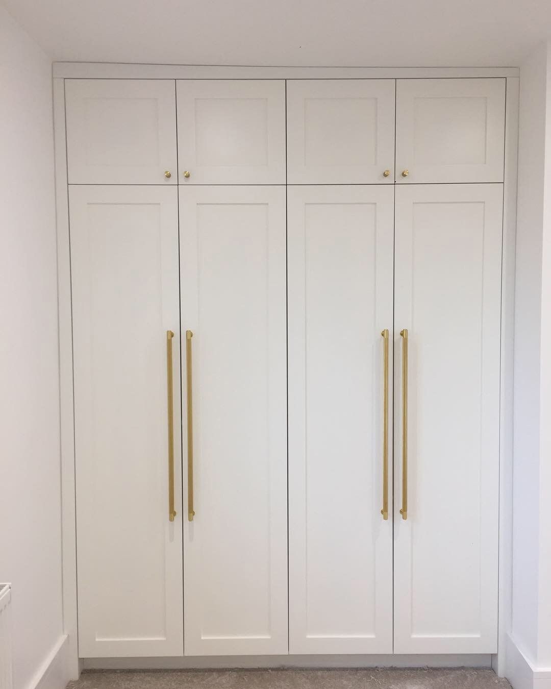 A closet with white cabinets and gold handles in a room.