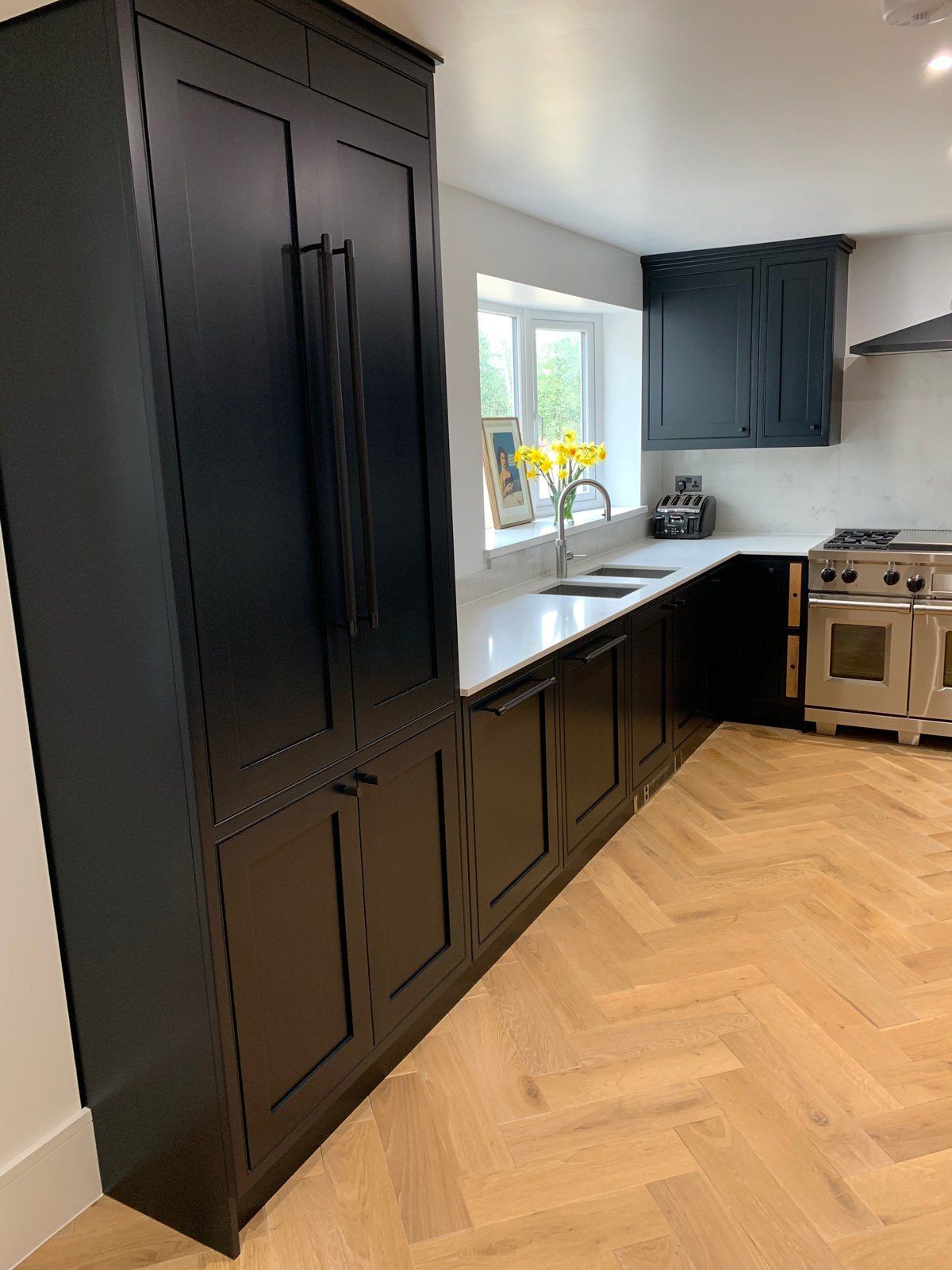 A kitchen with black cabinets , a stove , a sink , and a refrigerator.