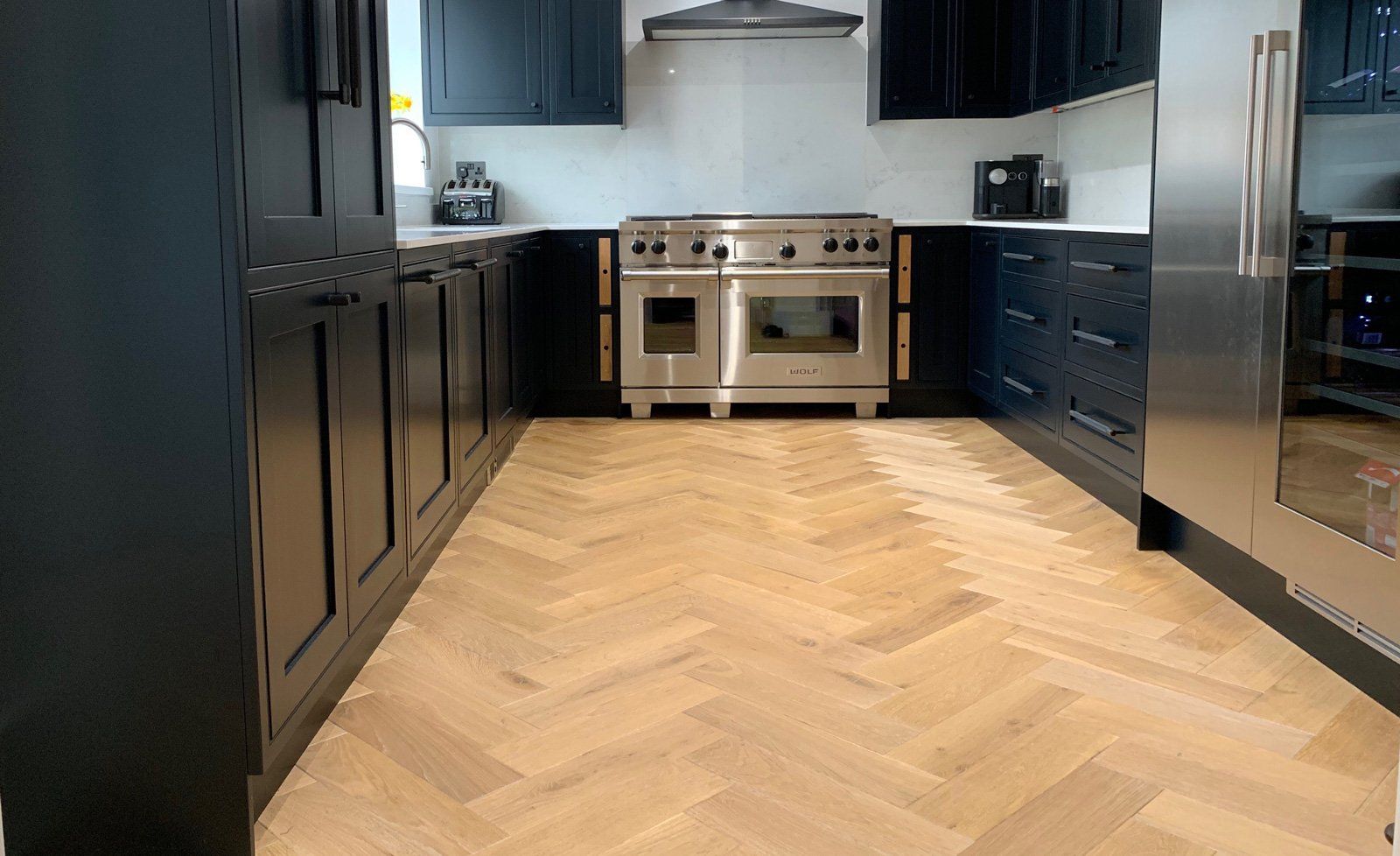 A kitchen with black cabinets and stainless steel appliances and a wooden floor.