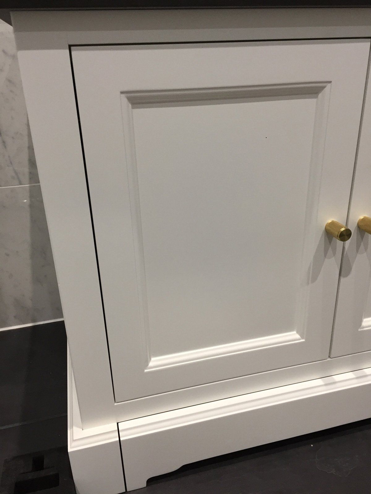 A close up of a white cabinet with gold handles in a bathroom.