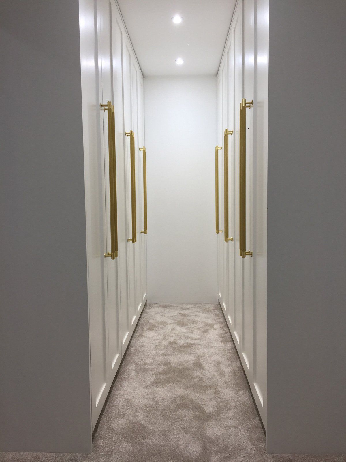 A walk in closet with white cabinets and gold handles.
