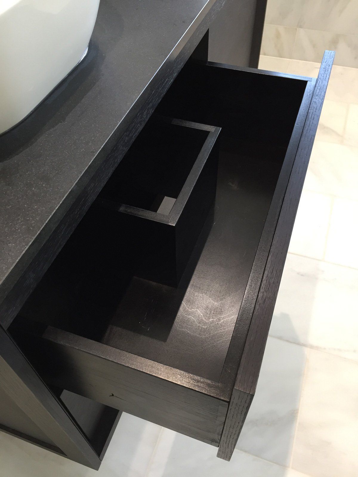 A black drawer in a bathroom with a sink in the background