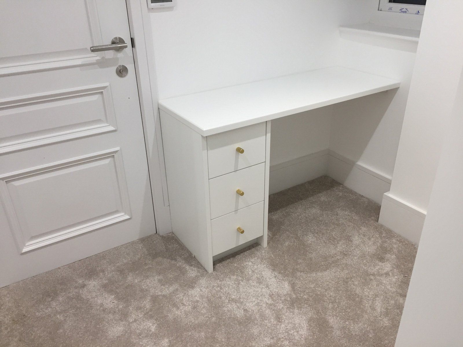 A white desk with three drawers in a room next to a door.