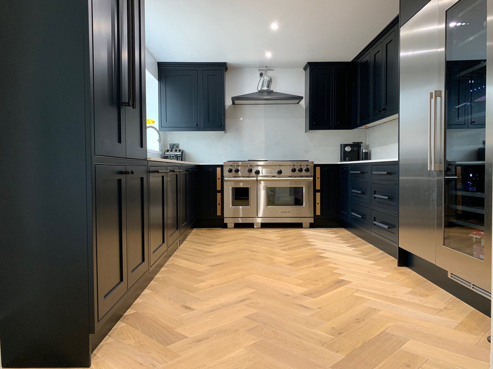 A kitchen with black cabinets and stainless steel appliances and a herringbone floor.