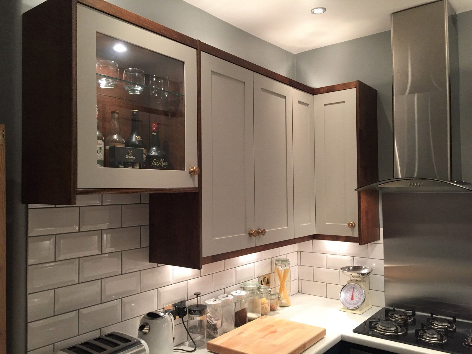 A kitchen with white cabinets , a stove , a cutting board , and a glass cabinet.