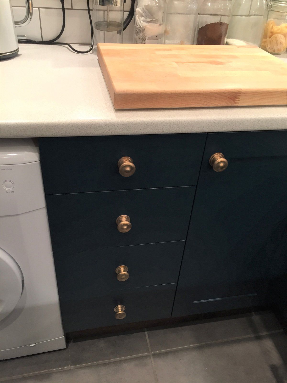 A wooden cutting board is sitting on top of a kitchen counter next to a washing machine.