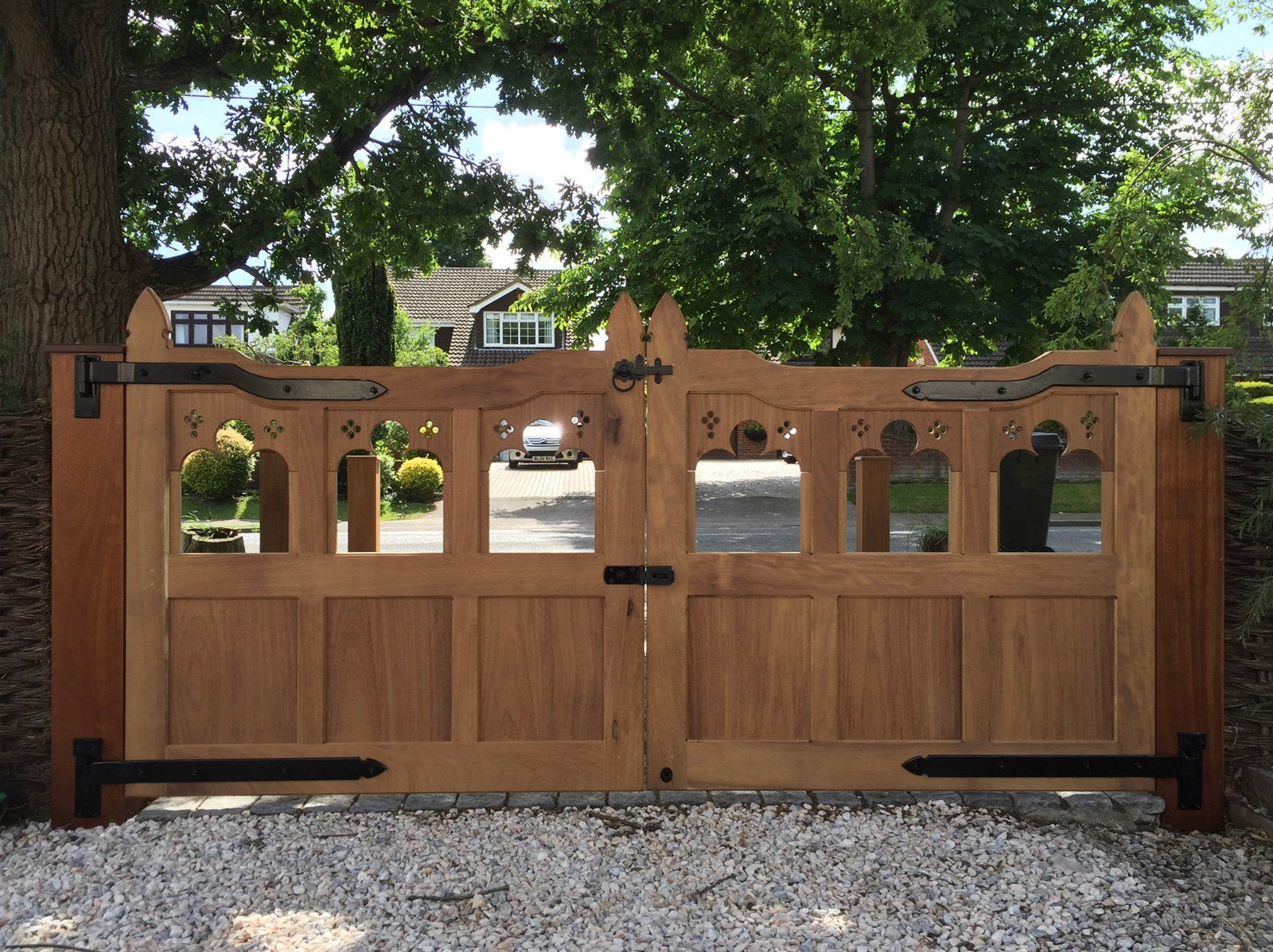 A wooden gate is open to a gravel driveway