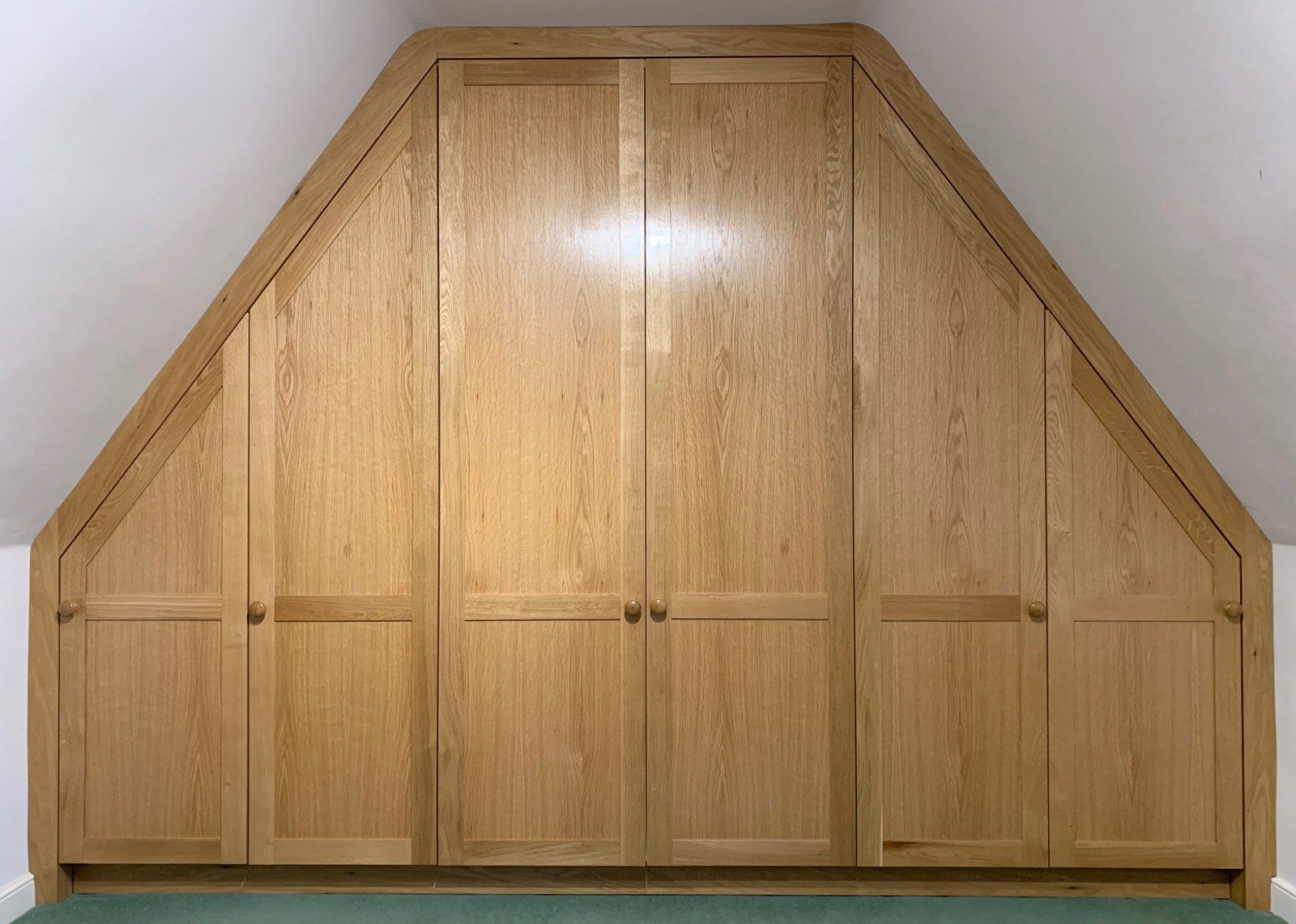 A wooden wardrobe with a slanted ceiling in a room.