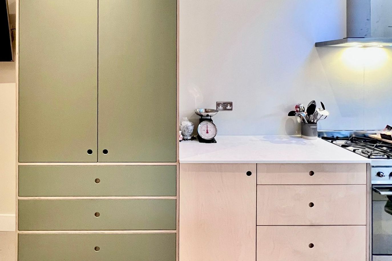 A kitchen with green cabinets and white drawers and a scale on the counter.