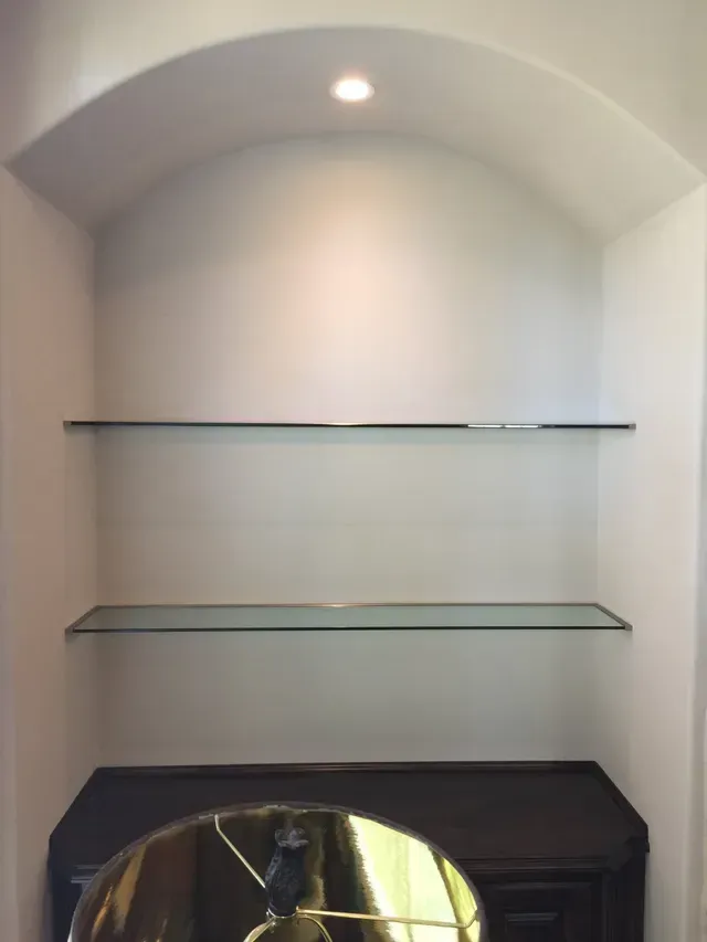 A lamp sits on a table next to a glass shelf