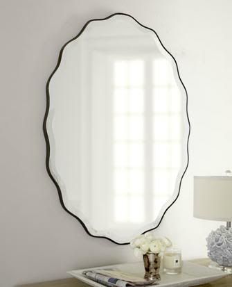 A large oval mirror with a black frame is hanging on a white wall.