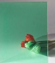 A green glass with a red rose reflected in it.