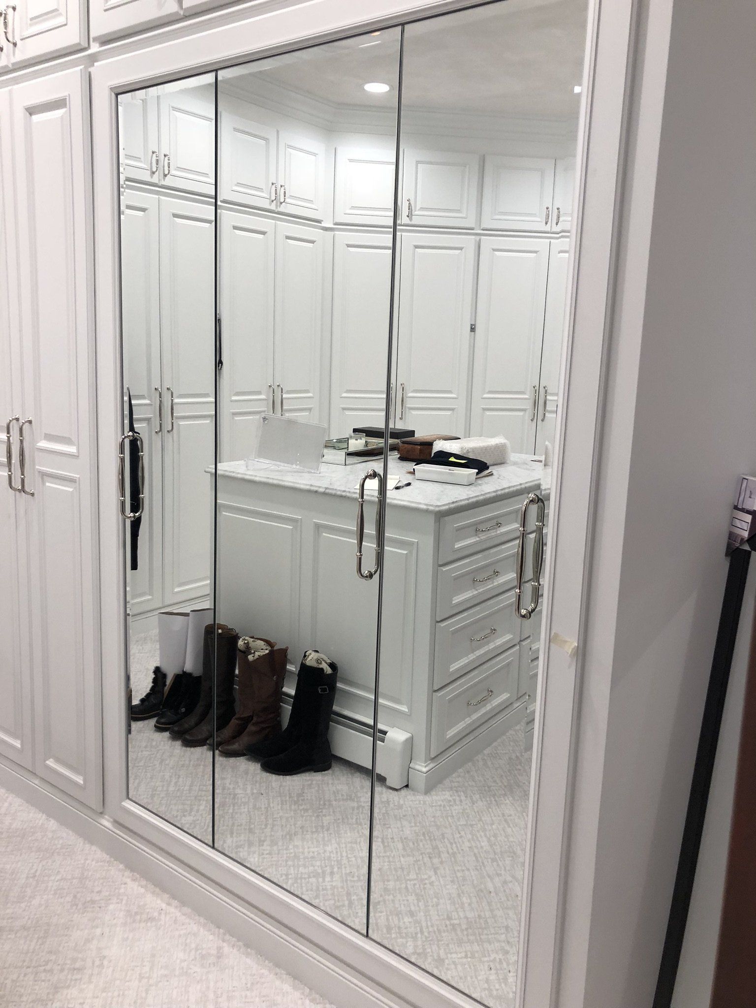 A walk in closet with white cabinets and mirrored doors.