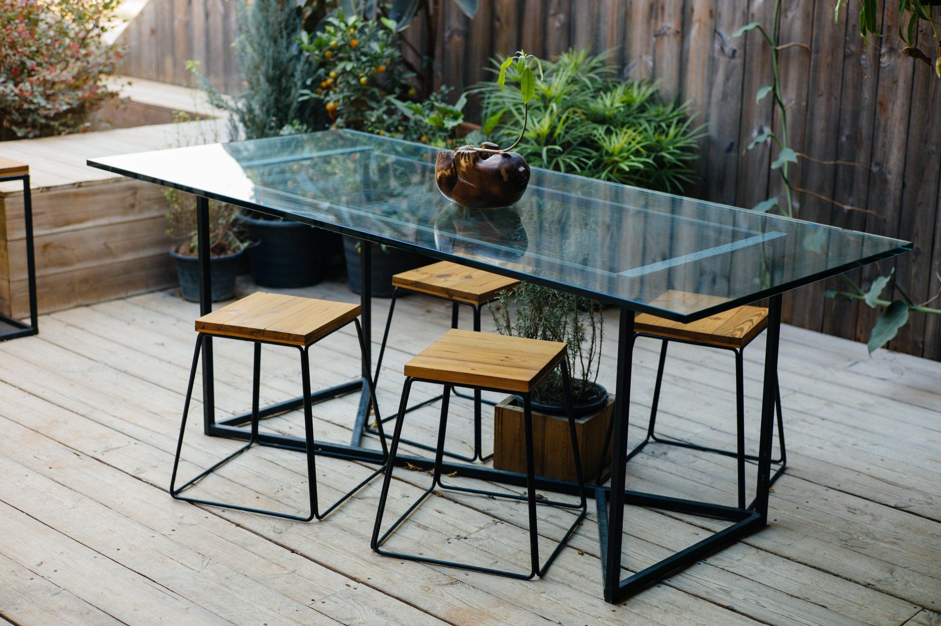 A glass table with stools on a wooden deck.