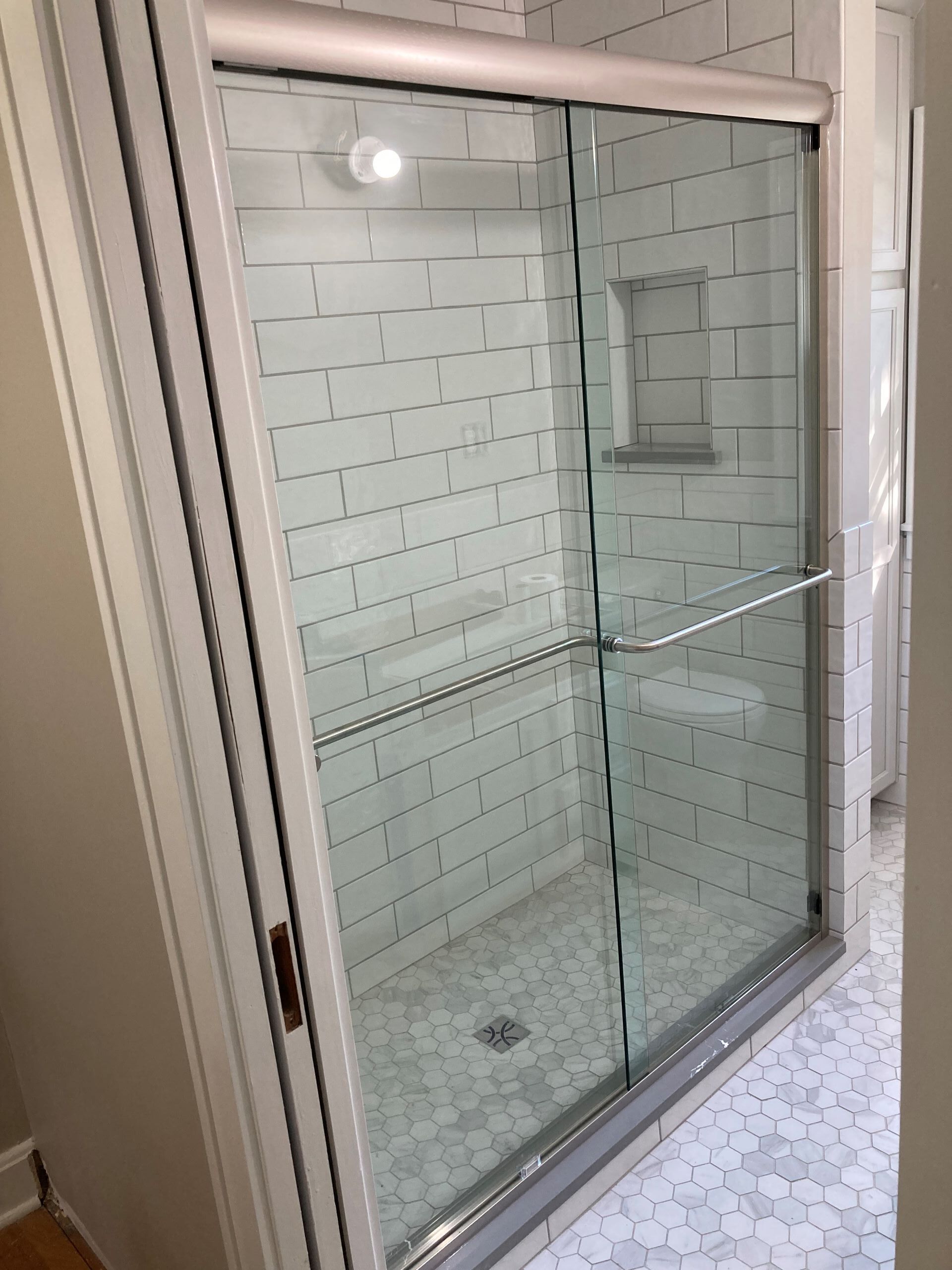A bathroom with a sliding glass shower door and white tiles.