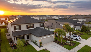 Electrician in yellow hard hat working on wiring panel mounted to a wall.