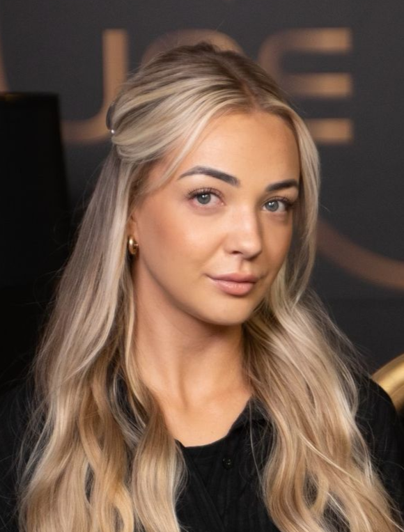 Woman with blonde hair, smiling, in front of a dark backdrop.