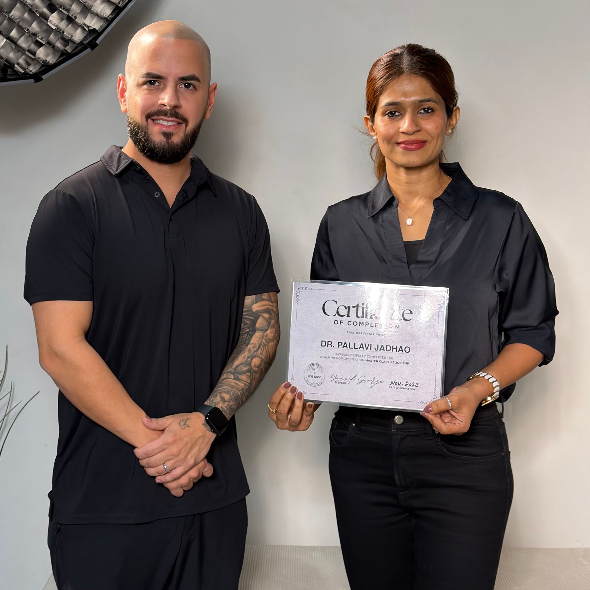 A man and a woman in black clothing pose, holding a certificate.