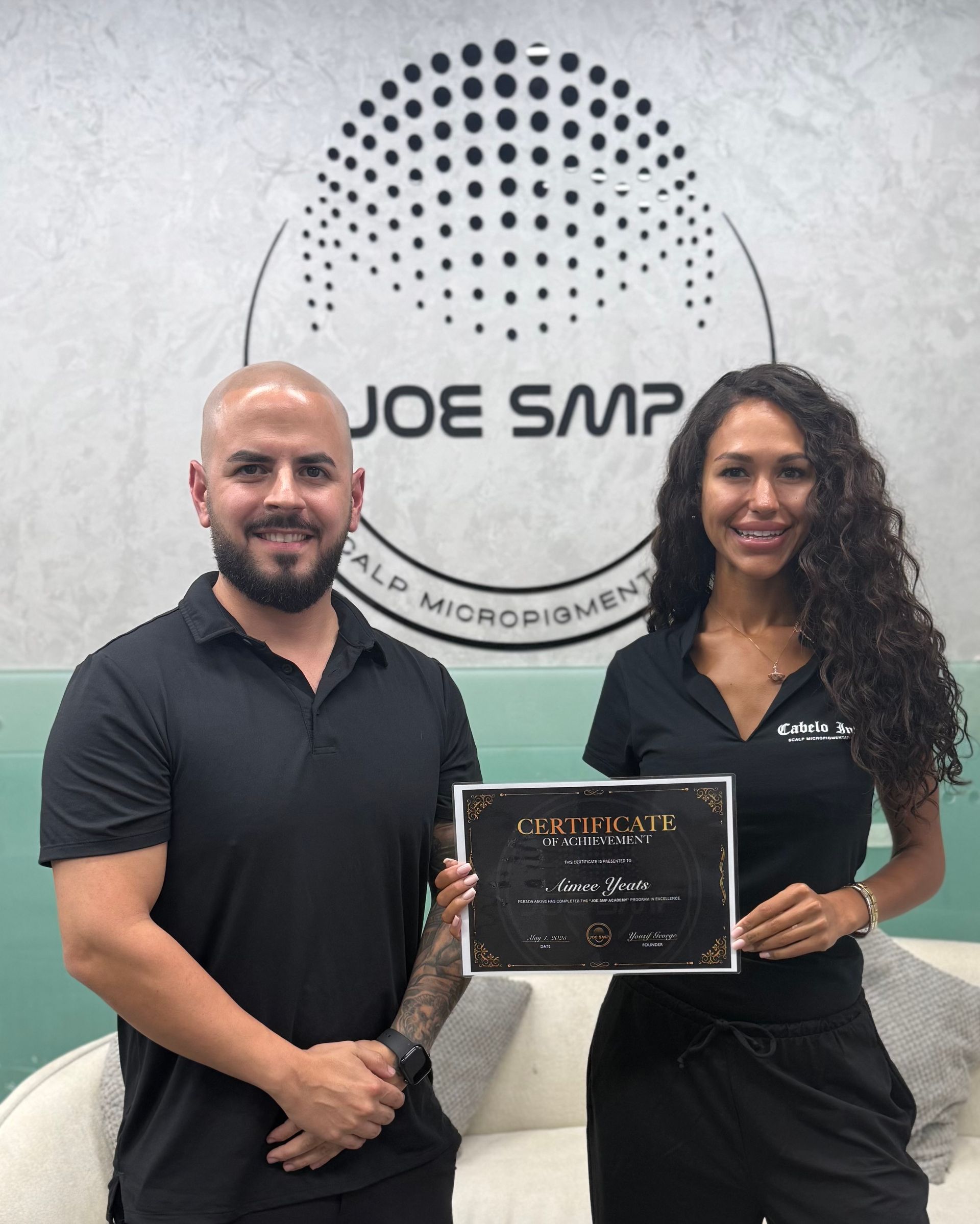 Two people holding a certificate, standing in front of a logo that says 