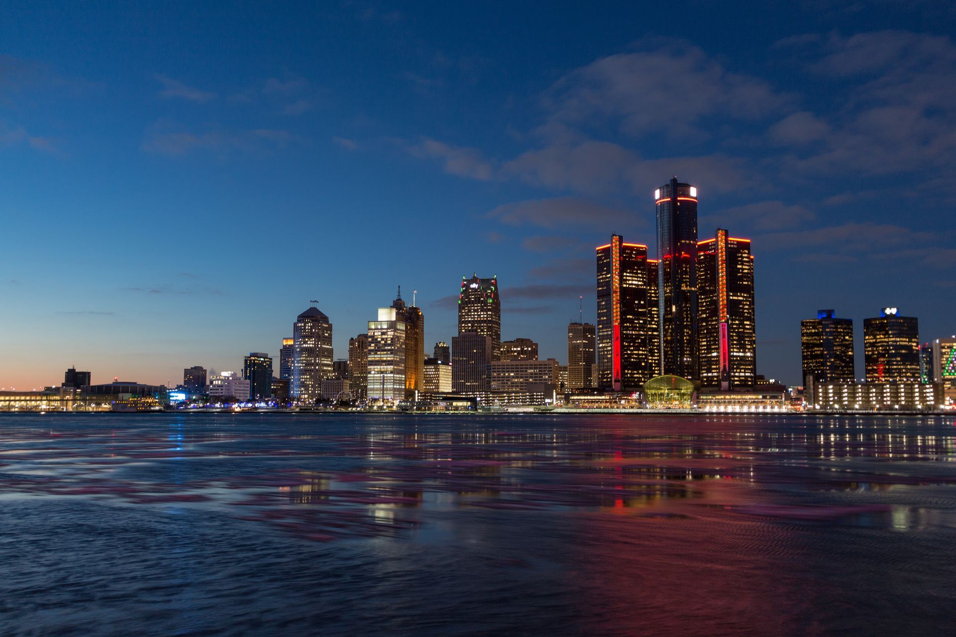 Detroit skyline at dusk with lights reflecting on the water.