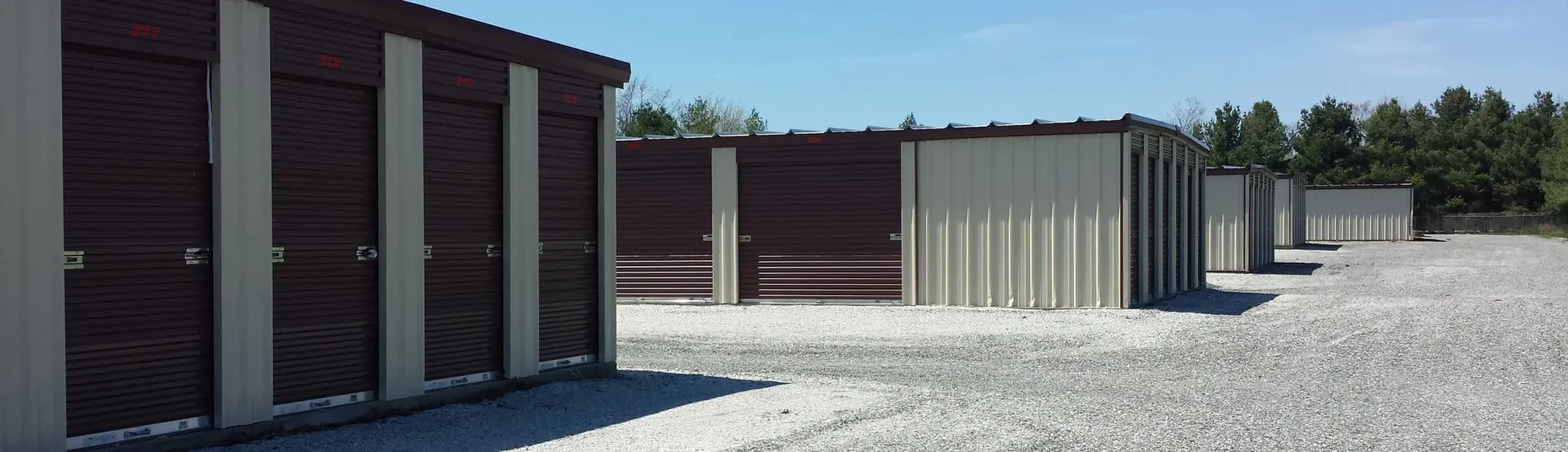 Storage units on a gravel lot with brown doors and white trim under a blue sky.