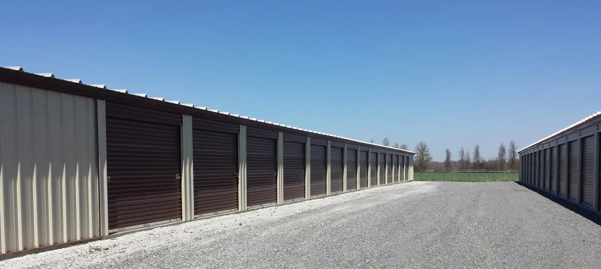 Storage units under a blue sky, with a gravel drive.