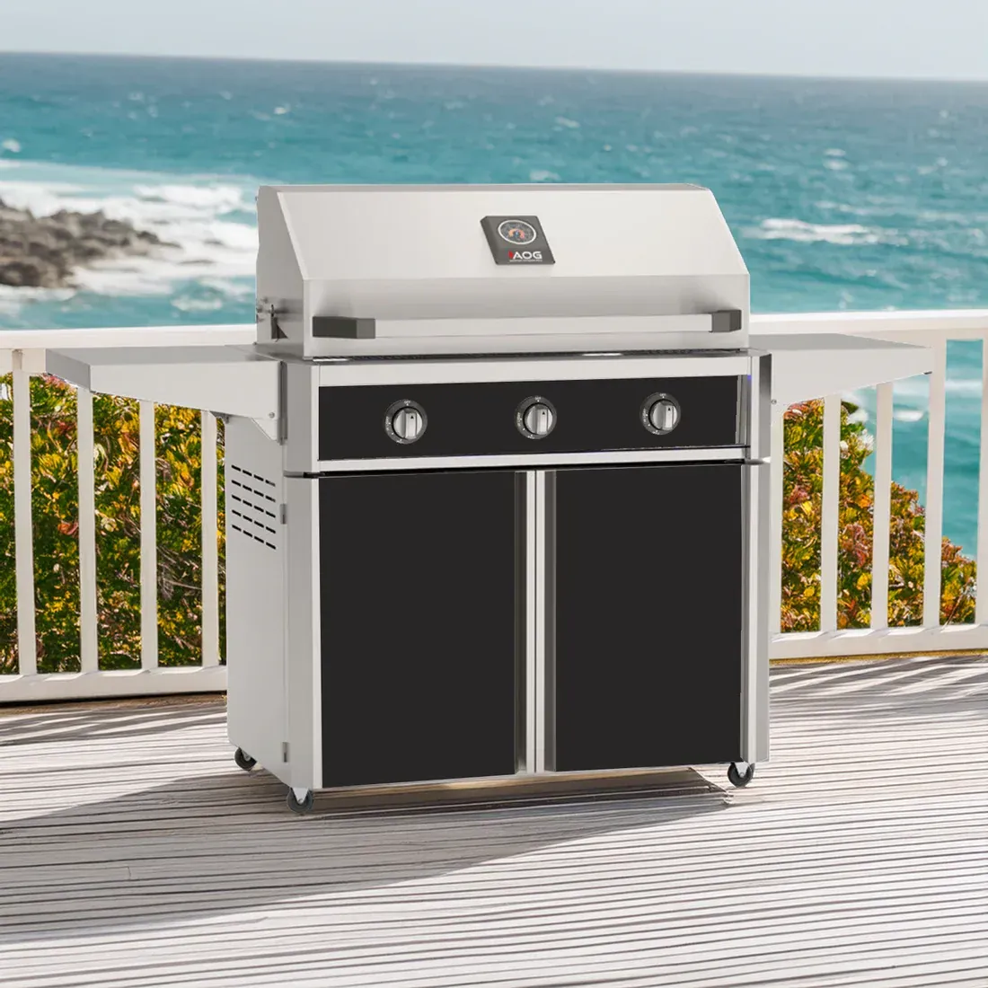 Stainless steel gas grill on a deck with a white railing and lush greenery in the background.