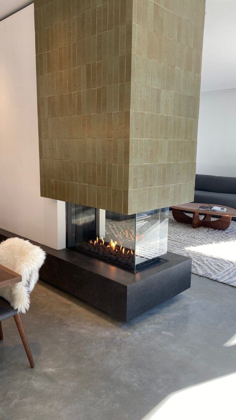 Fireplace with lit flames, set in a stone wall. A marble shelf supports art and decor; a living room setting.