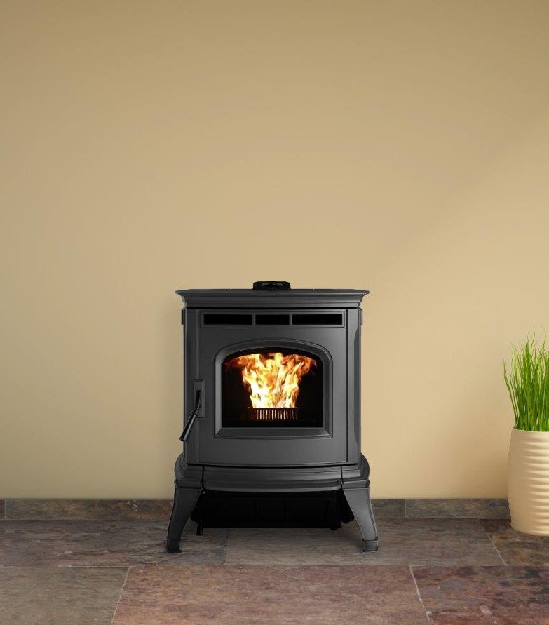 Black pellet stove with flames against a cream wall, sitting on a tiled floor. A potted plant is to the right.