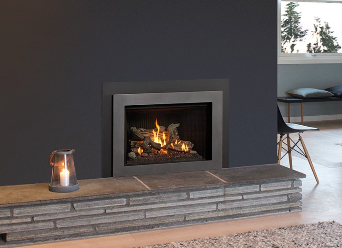 A modern fireplace with a lit fire in a dark gray wall. A stone hearth holds a lantern.