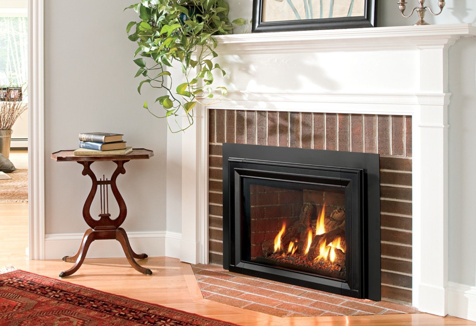 A gas fireplace with flames burning brightly, framed by a black border and brick. A white mantelpiece and a small side table are also present.