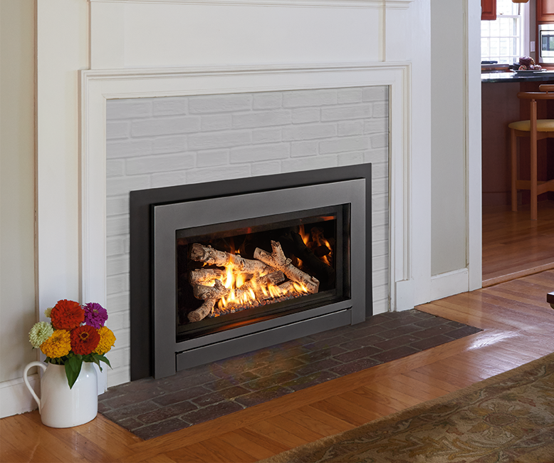Fireplace with burning logs, surrounded by a gray frame and a white brick-like background. A vase of flowers sits on the left.