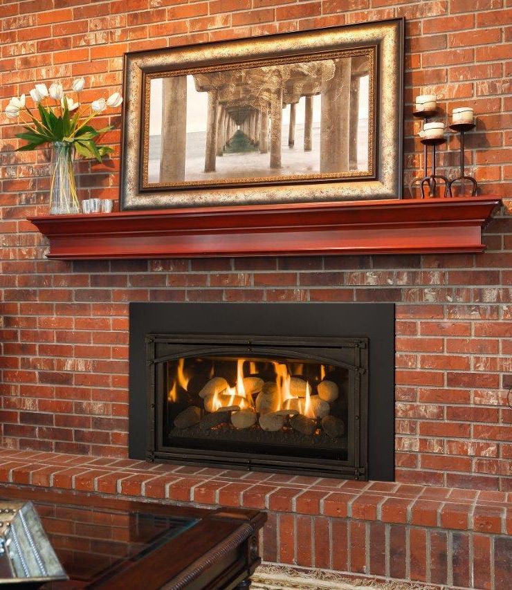 A fireplace with a burning fire, framed by a brick wall. Above, a mantel displays a framed photograph and decorative candles.
