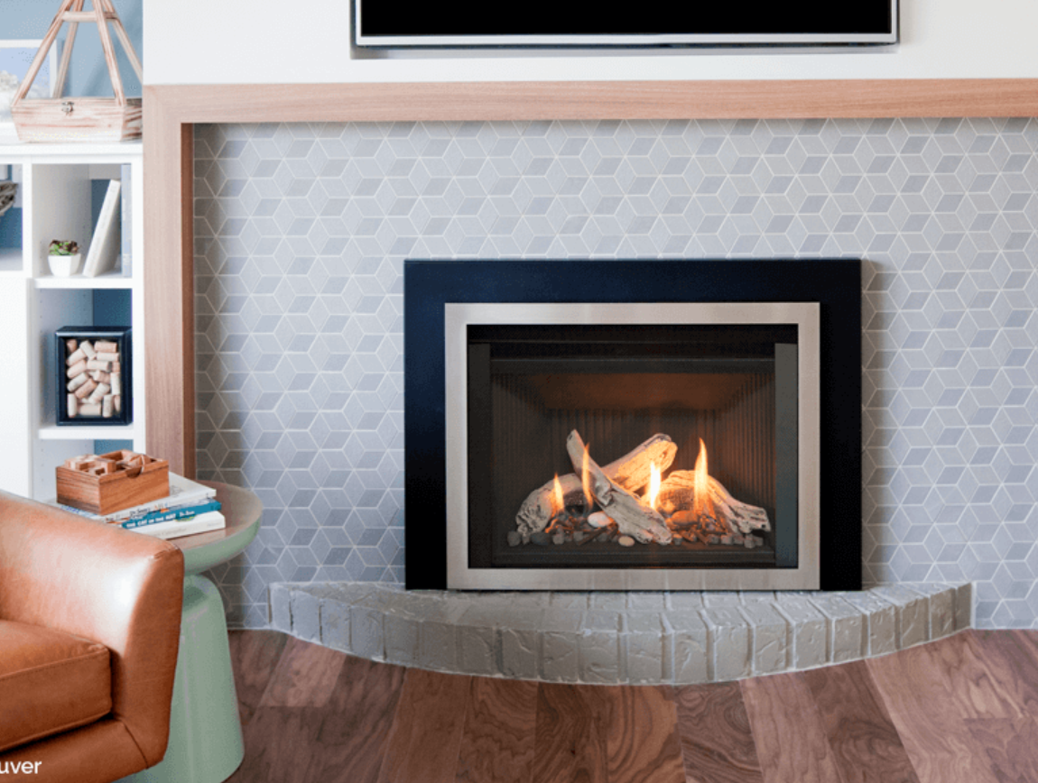 Fireplace with a black and silver frame, lit flames, set against a geometric tiled wall, integrated into a corner with a brown leather armchair.