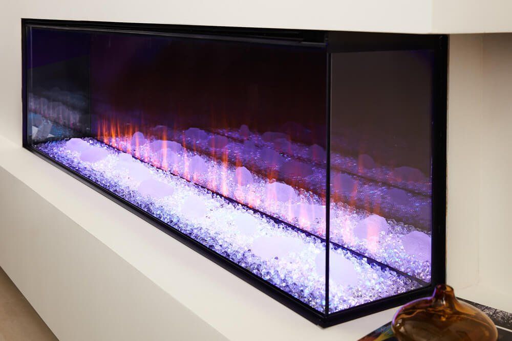 Modern electric fireplace with a glass front, showing purple and orange flames over white crystals, set in a white wall.