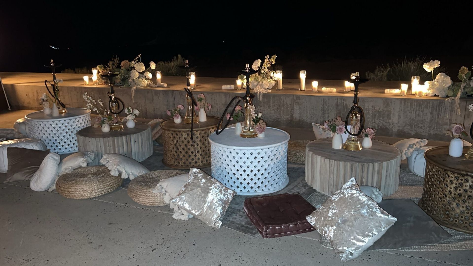 A row of tables with hookahs and candles on them at night.