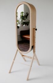 A wooden full length mirror is sitting on a white surface.