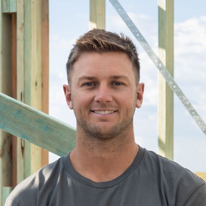 A Blonde Man Wearing a Ridgeline T-shirt is Smiling in Front of a Wooden Structure — Ridgeline Building Co In Gerringong, NSW