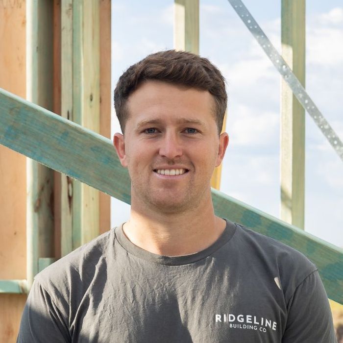 A Brunette Man Wearing a Ridgeline T-shirt is Smiling in Front of a Wooden Structure — Ridgeline Building Co In Gerringong, NSW