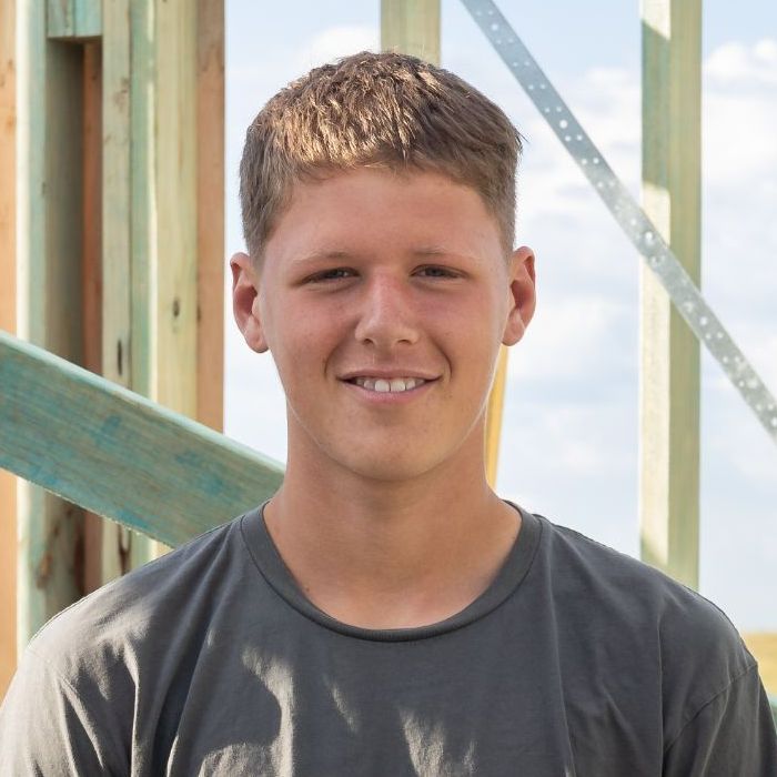A Young Man Wearing a Ridgeline T-shirt is Smiling in Front of a Wooden Structure — Ridgeline Building Co In Gerringong, NSW