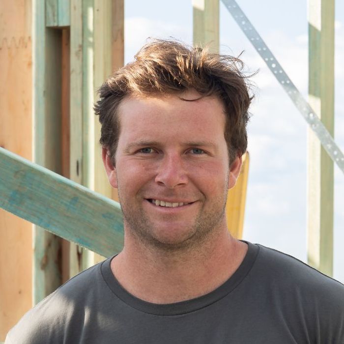 Man Wearing a Ridgeline T-shirt is Smiling in Front of a Wooden Structure — Ridgeline Building Co In Gerringong, NSW