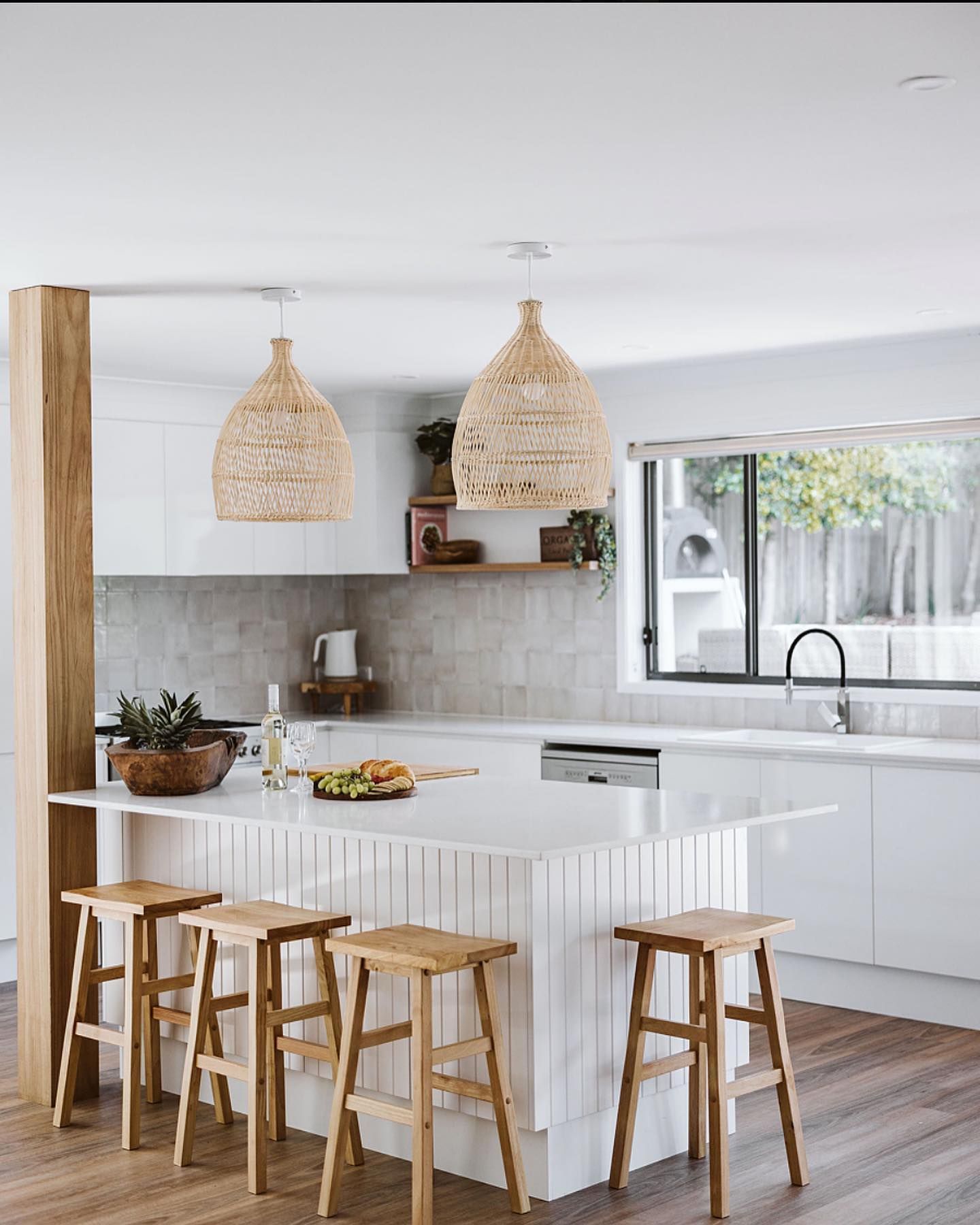 Bright White Kitchen With a Marble Island, Wood Stools, and Woven Pendant Lights