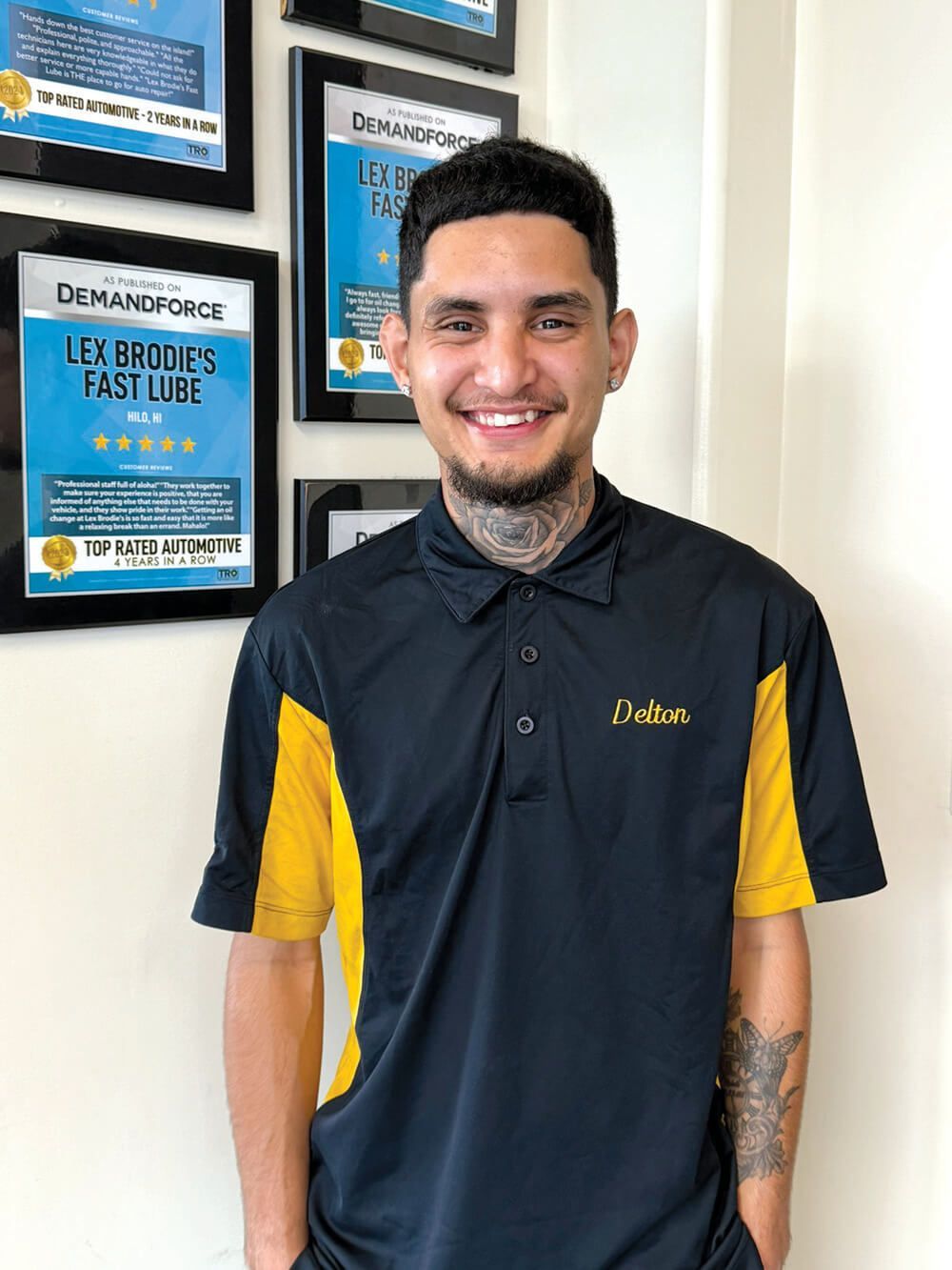 A man wearing a black and yellow polo shirt is standing in front of a wall.
