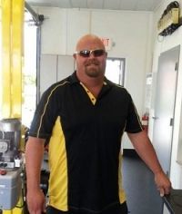 A man wearing sunglasses and a black and yellow shirt is standing in a room.