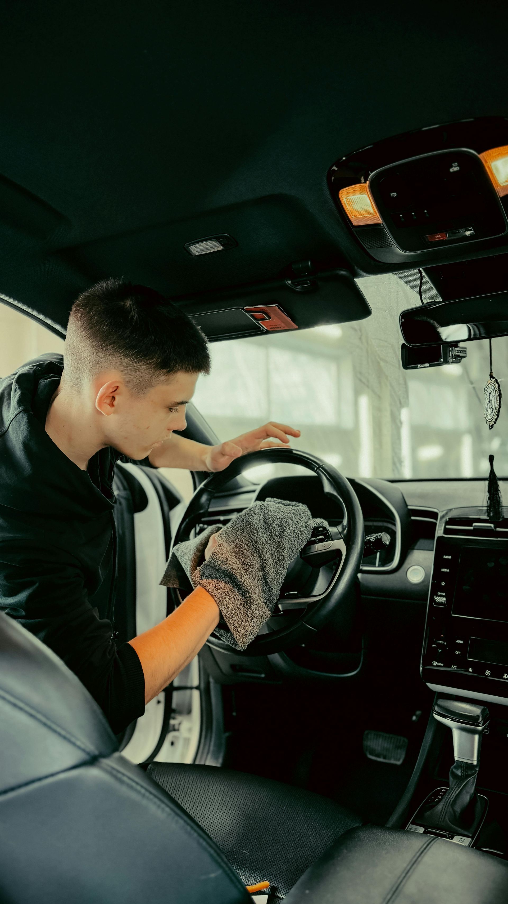 A man is cleaning the steering wheel of a car with a cloth.