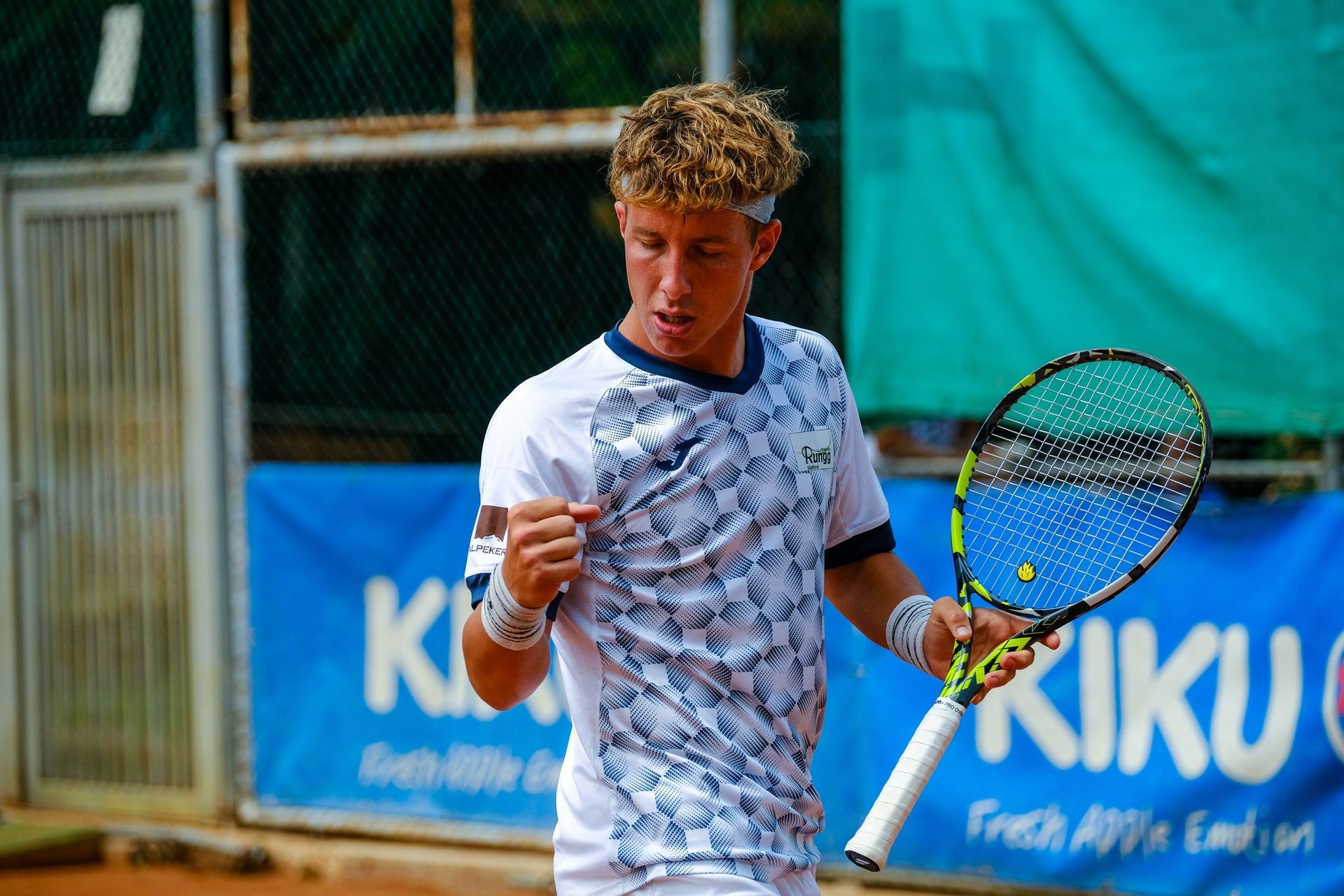 A young man is holding a tennis racquet in front of a banner that says kiku