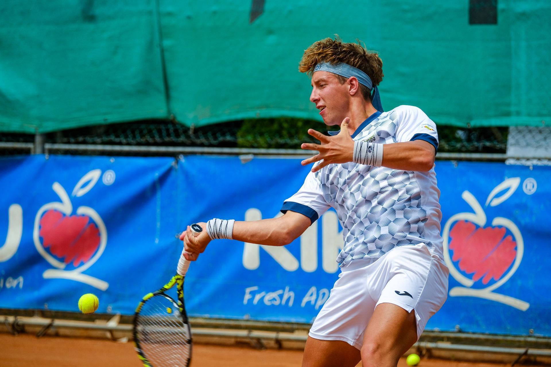 A man is playing tennis in front of a banner that says fresh apple